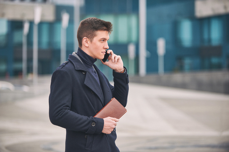 Young business man with notepad and mobile phone near of modern building.の写真素材