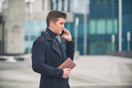 Young business man with notepad and mobile phone near of modern building.の写真素材