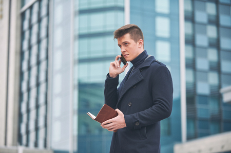 Young business man with notepad and mobile phone near of modern building.の写真素材