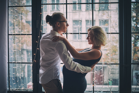 Man and pregnant woman dance near window in loft style roomの写真素材