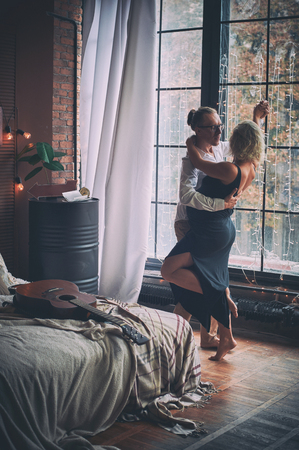 Man and pregnant woman dance near window in loft style roomの写真素材