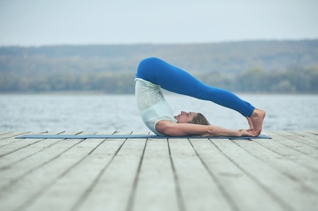 Beautiful young woman practices yoga asana Shirshasana - Headstand pose on the wooden deck near the lakeの写真素材