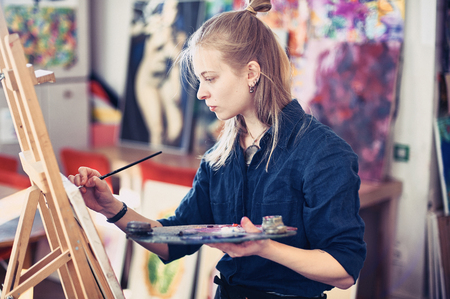 Young Woman Artist Working On Painting In Studio. Selective focus on foreground.の写真素材