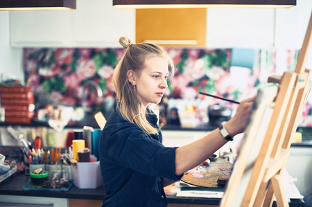 Young Woman Artist Working On Painting In Studio. Selective focus on foreground.の写真素材