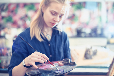 Young Woman Artist Working On Painting In Studio. Selective focus on foreground.の写真素材