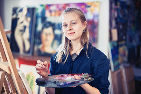 Young Woman Artist Working On Painting In Studio. Selective focus on foreground.の写真素材