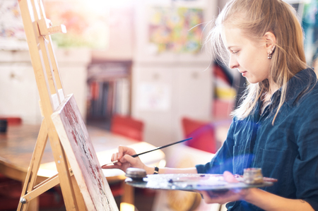 Young Woman Artist Working On Painting In Studio. Selective focus on foreground.の写真素材