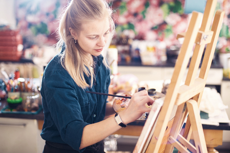 Young Woman Artist Working On Painting In Studio. Selective focus on foreground.の写真素材