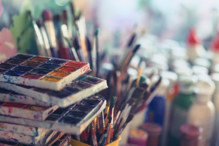 Paint brushes and watercolor paints on the table in a workshop, selective focus, close up.の写真素材