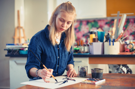 Young Woman Artist Working On Painting In Studio. Selective focus on foreground.の写真素材