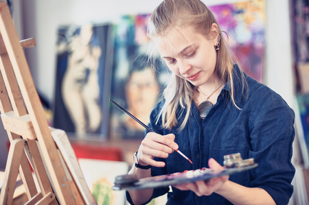 Young Woman Artist Working On Painting In Studio. Selective focus on foreground.の写真素材