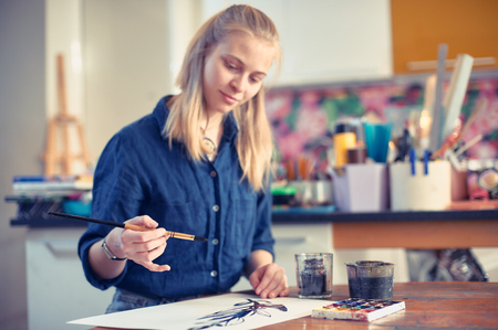 Young Woman Artist Working On Painting In Studio. Selective focus on foreground.の写真素材