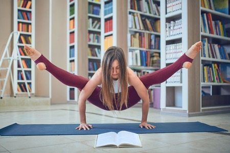 Beautiful woman reading book and practices handstand yoga asana Tittibhasana - firefly pose in the libraryの写真素材