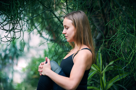 Beautiful young woman practices yoga asana in jungle. Sunny dayの写真素材