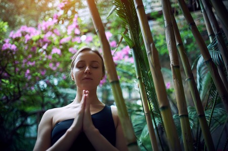 Portrait of cute young woman meditating and doing namaste hand in jungle. Sunny dayの写真素材