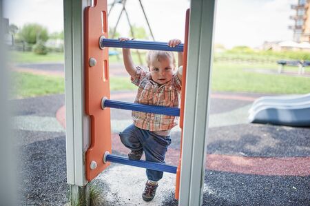 Happy 1 year old toddler climbs on the slide on the playground.