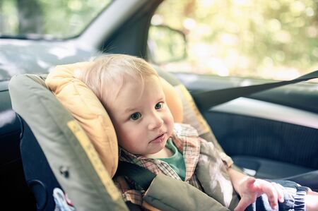 Portrait of pretty 1 year old toddler boy sitting in car safety seat mounted in the front seat. Child transportation safety. Warning labels on the chair are not trademarked.の写真素材