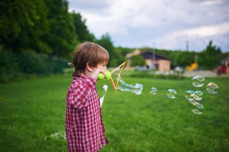 Outdoors portrait of cute preschool boy blowing soap bubbles on a green lawn at the playgroundの写真素材