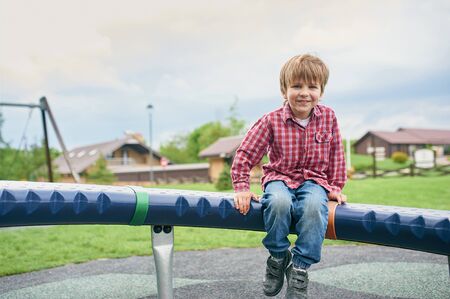 Outdoors portrait of cute preschool smiling boy swinging on a swing at the playground.