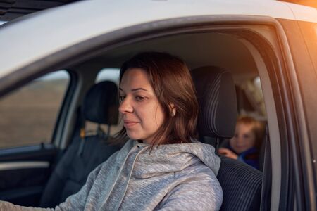 Mother drives a car, a child in a safety seat in the rear seat.