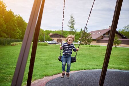 Outdoors portrait of cute preschool laughing boy swinging on a swing at the playground.の写真素材