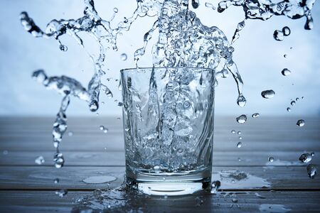 water to drink poured into a glass on blue background studio shotの写真素材