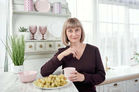 Portrait of a beautiful mature woman sitting in the modern kitchen.の写真素材
