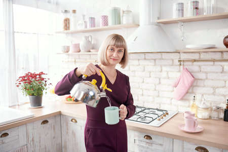 Portrait of a beautiful mature woman sitting in the modern kitchen.の写真素材
