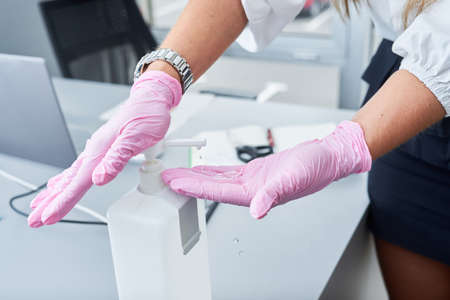 Businesswoman with face mask and gloves using hand sanitizer in the office. Corona virus protection.