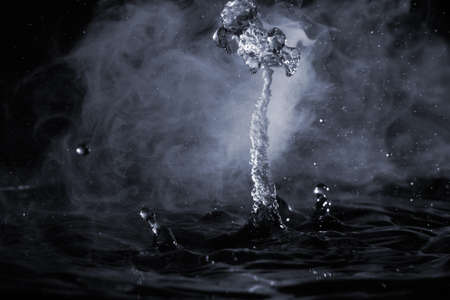 Boiling water splash with steam on black background closeup.の写真素材