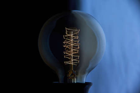 Electric vintage Edison light bulb with a spiral on a blue background. Retro style lamp.