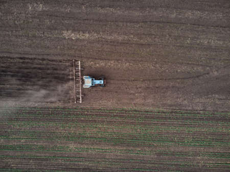 Agricultural tractor plows soil field for sowing, aerial top view from the drone. Spring farming...