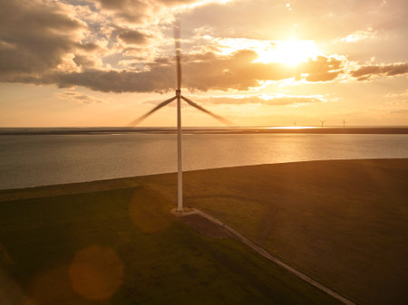 Aerial top view of wind turbines and agriculture field near the sea at sunset