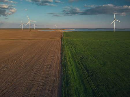 Aerial top view of wind turbines and agriculture field near the sea at sunset