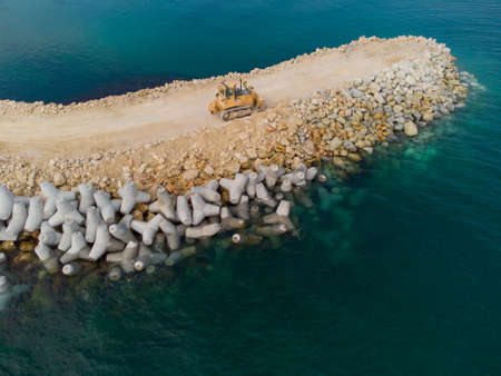 Aerial top view of breakwater construction. Bulldozer on a pile of boulders in the sea