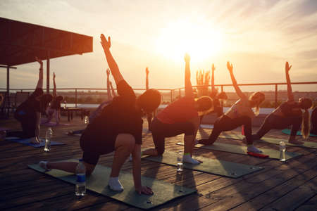 Silhouette of men and women doing yoga outdoor on the roof at sunsetの写真素材
