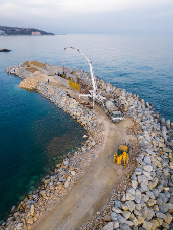 Heavy construction equipment is building a breakwater. Pouring concrete on a pier under construction in the sea. aerial view.の写真素材