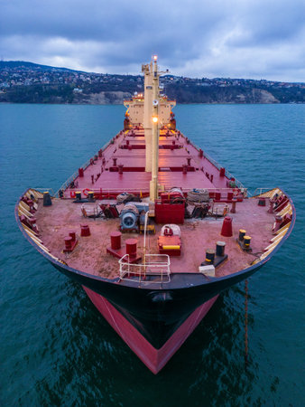 aerial view of a bulk carrier at evening showcases a stunning display of lights reflecting off the water as the massive vessel cuts through the waves. The contrast between the darkness of the ocean and the brightly lit ship creates a captivating and atmospheric scene.の写真素材
