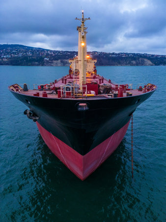 aerial view of a bulk carrier at evening showcases a stunning display of lights reflecting off the water as the massive vessel cuts through the waves. The contrast between the darkness of the ocean and the brightly lit ship creates a captivating and atmospheric scene.の写真素材