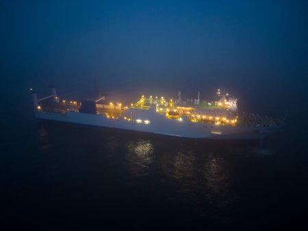 Aerial view of a ferryboat navigating through foggy conditions at night on the sea. The combination of the dark setting, the foggy conditions, and the presence of the ferryboat can create an eerie and potentially treacherous environment that requires careful navigation and attention to safety measures.の写真素材