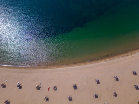 aerial view of a sandy deserted beach with straw umbrellas, a red sea kayak and a calm turquoise seaの写真素材
