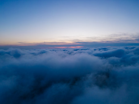 A drone flies over fluffy clouds at sunset. The drone flies through the clouds, creating a sense of wonder and aweの写真素材