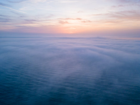 Aerial view of a sunrise sea with a blanket of morning fog and morning sunbeams shining throughの写真素材