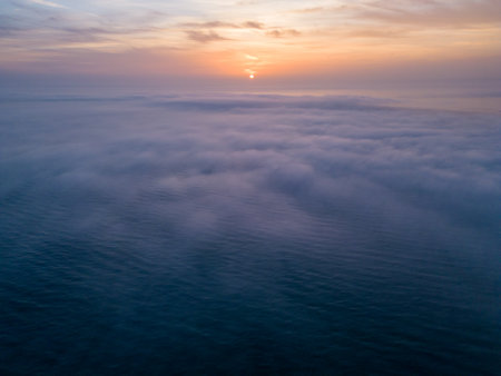 Aerial view of a sunrise sea with a blanket of morning fog and morning sunbeams shining throughの写真素材