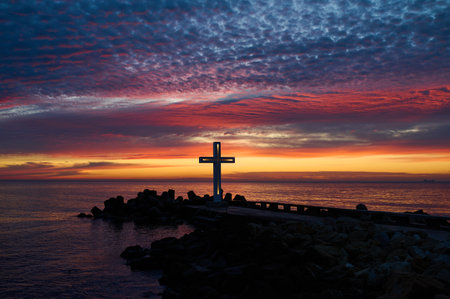 Christian Holy cross early in the morning at sunrise. The large cross stands on the edge of a breakwater on the sea coastの写真素材