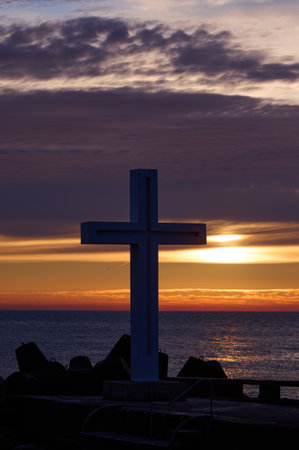 Christian Holy cross early in the morning at sunrise. The large cross stands on the edge of a breakwater on the sea coastの写真素材