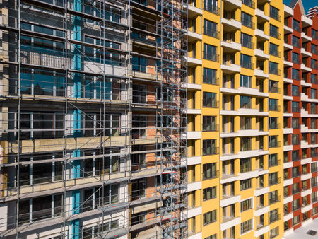 Drone flight along the facade of a modern apartment building under construction surrounded by scaffoldingの写真素材
