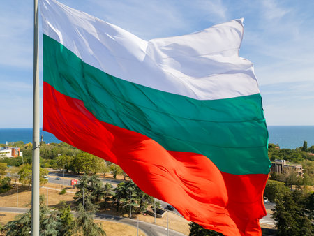 The Bulgarian flag waves proudly above a coastal city, with the vast sea and green landscape in the...