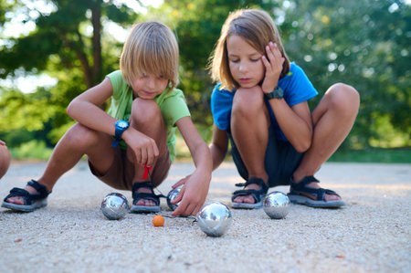 Two children measure the distance between petanque balls and the target ball during a game. A focused and playful moment in an outdoor setting on a sunny dayの写真素材