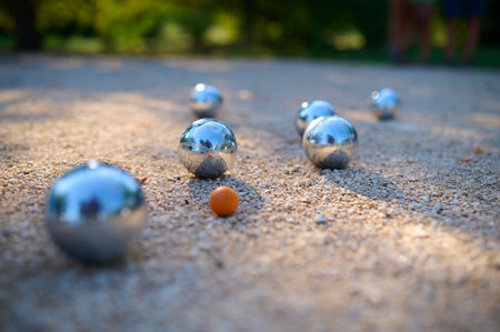 Close-up of petanque balls scattered on gravel with the target ball in focus. The shiny metal balls reflect sunlight, capturing a playful outdoor moment in a park settingの写真素材